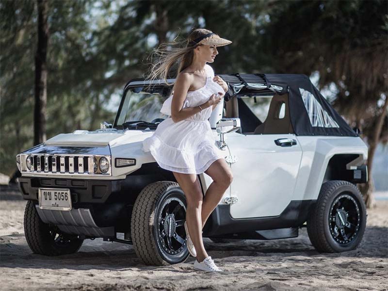 woman standing next to white electric hummer on beach